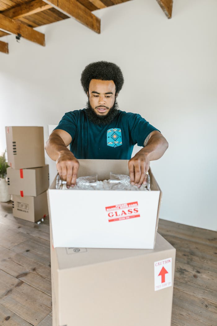 Adult man carefully packing fragile glassware in a moving box. Ideal for moving services.